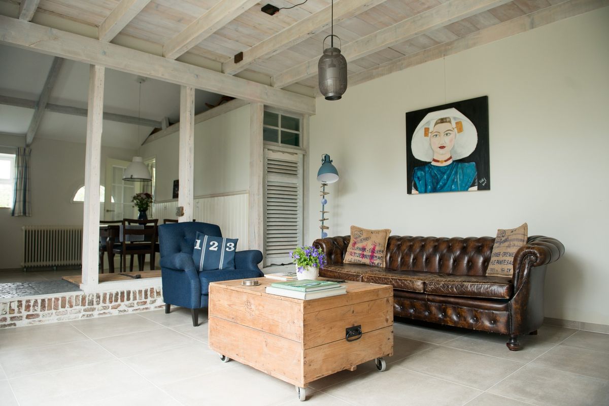 Salón con sofá Chesterfield de cuero, sillón azul y vigas de madera vistas – Zeeuwshuisje casa de vacaciones, Koudekerke