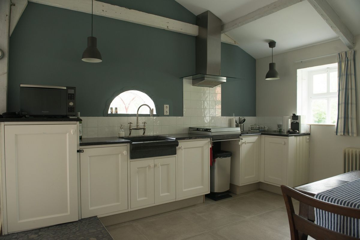 Cocina completa con muebles blancos, campana de acero inoxidable y paredes verde oscuro – Zeeuwshuisje casa de vacaciones, Koudekerke