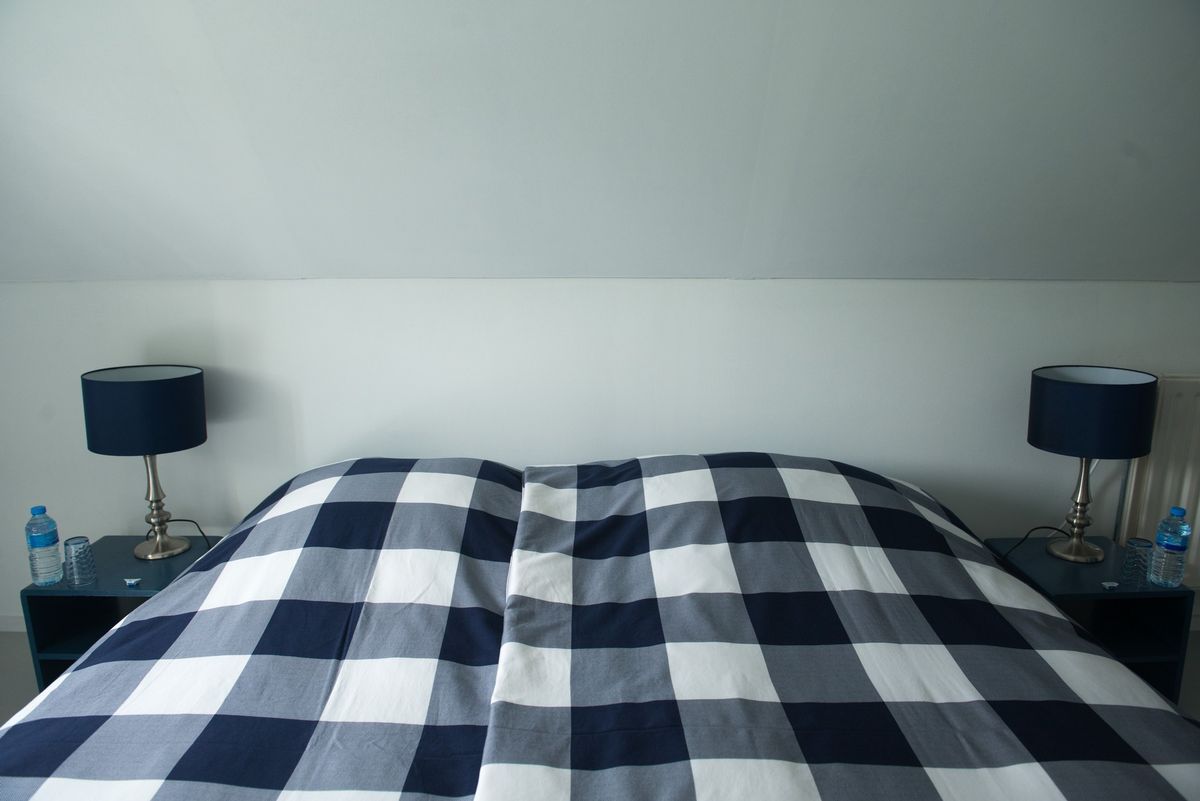 Cama doble de la habitación principal con edredón a cuadros marino y lámparas de mesita a juego – Zeeuwshuisje casa de vacaciones, Koudekerke