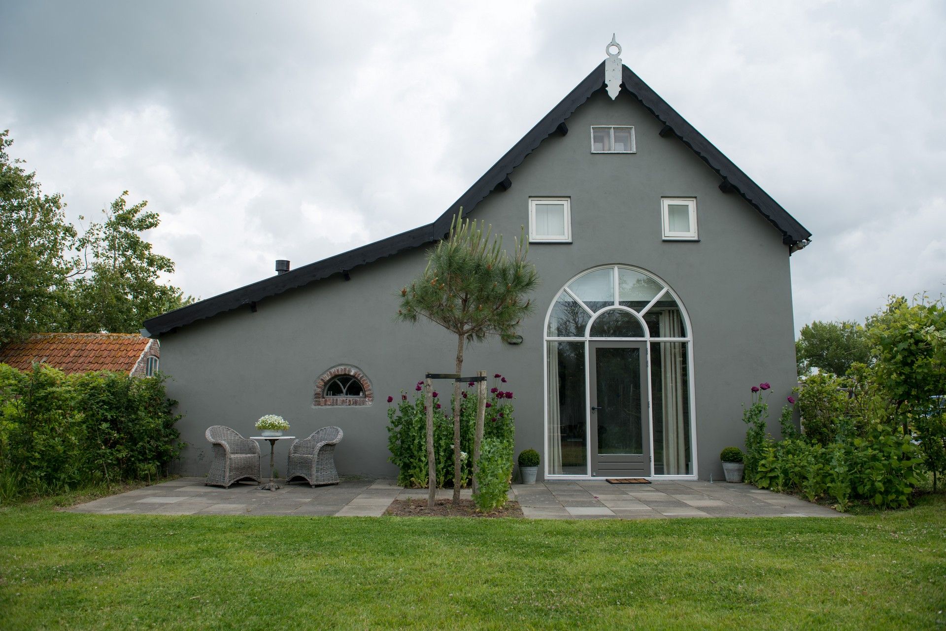 Front exterior of the converted barn holiday home with arched window and terrace – Zeeuwshuisje, Koudekerke